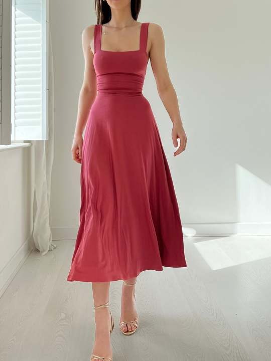 Frau trägt ein rosa ärmelloses Midikleid mit tailliertem Oberteil und weitem Rock.