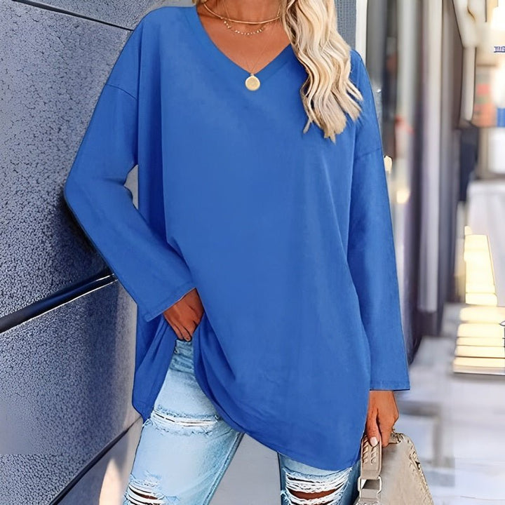 Frau trägt ein blaues Langarmshirt mit V-Ausschnitt und eine Hand in der Tasche